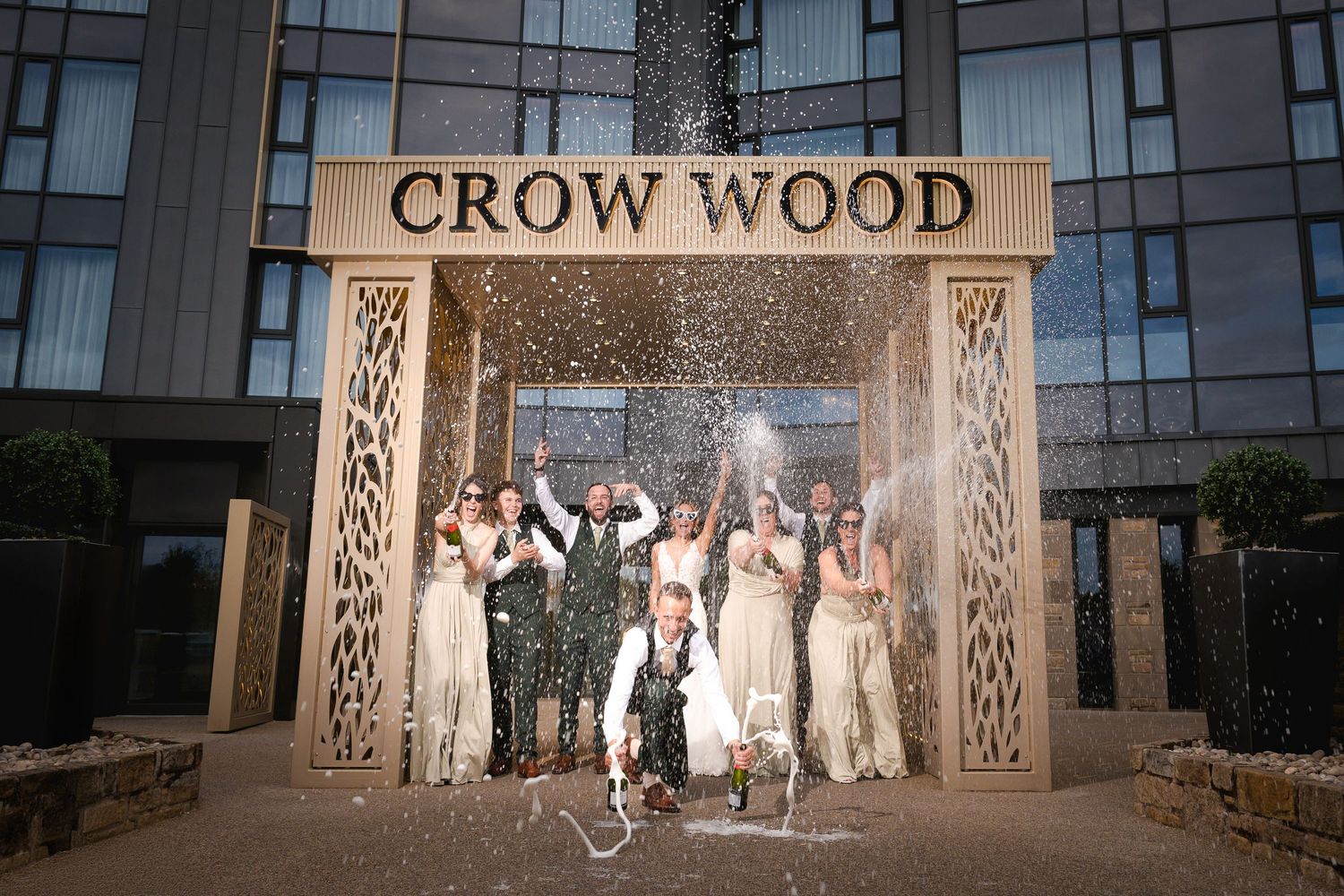 Illuminated wooden archway entrance with 'CROW WOOD' text and people standing beneath intricate carved designs.