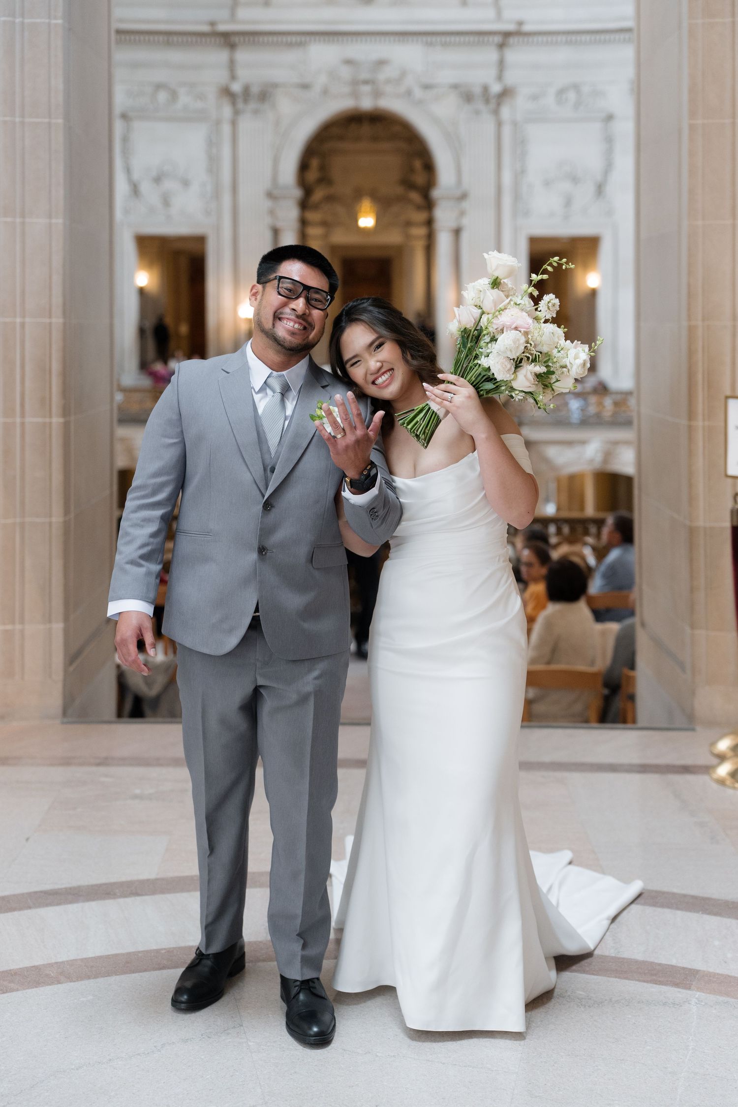 Happy newlyweds show off their playful personality posing in a grand marble hallway at their city hall wedding.