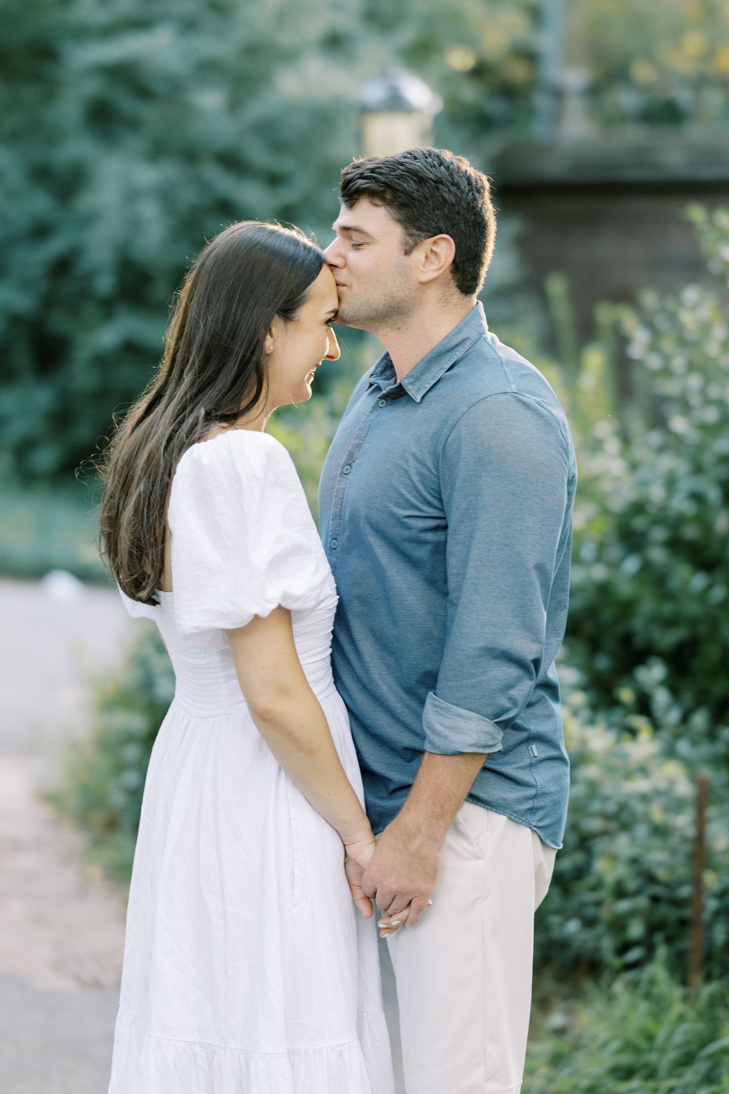 A romantic couple in white and blue casual attire shares intimate moments in a garden setting.