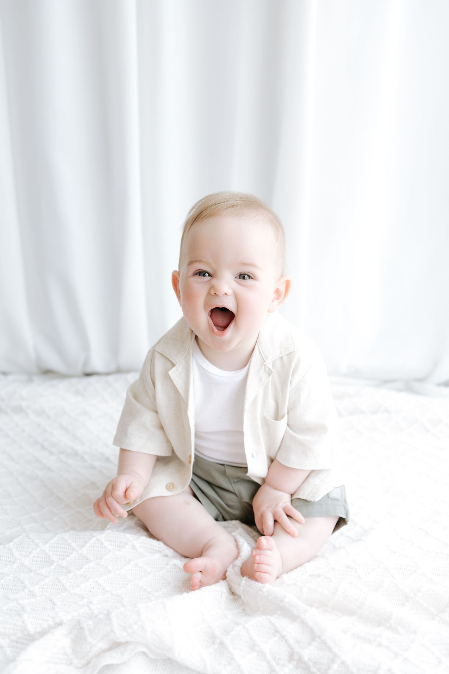 A tiny newborn baby wearing a white onesie lying peacefully on soft white bedding.