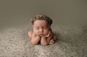 Adorable newborn baby peacefully sleeping in fetal position on soft grey textured backdrop during professional photoshoot.