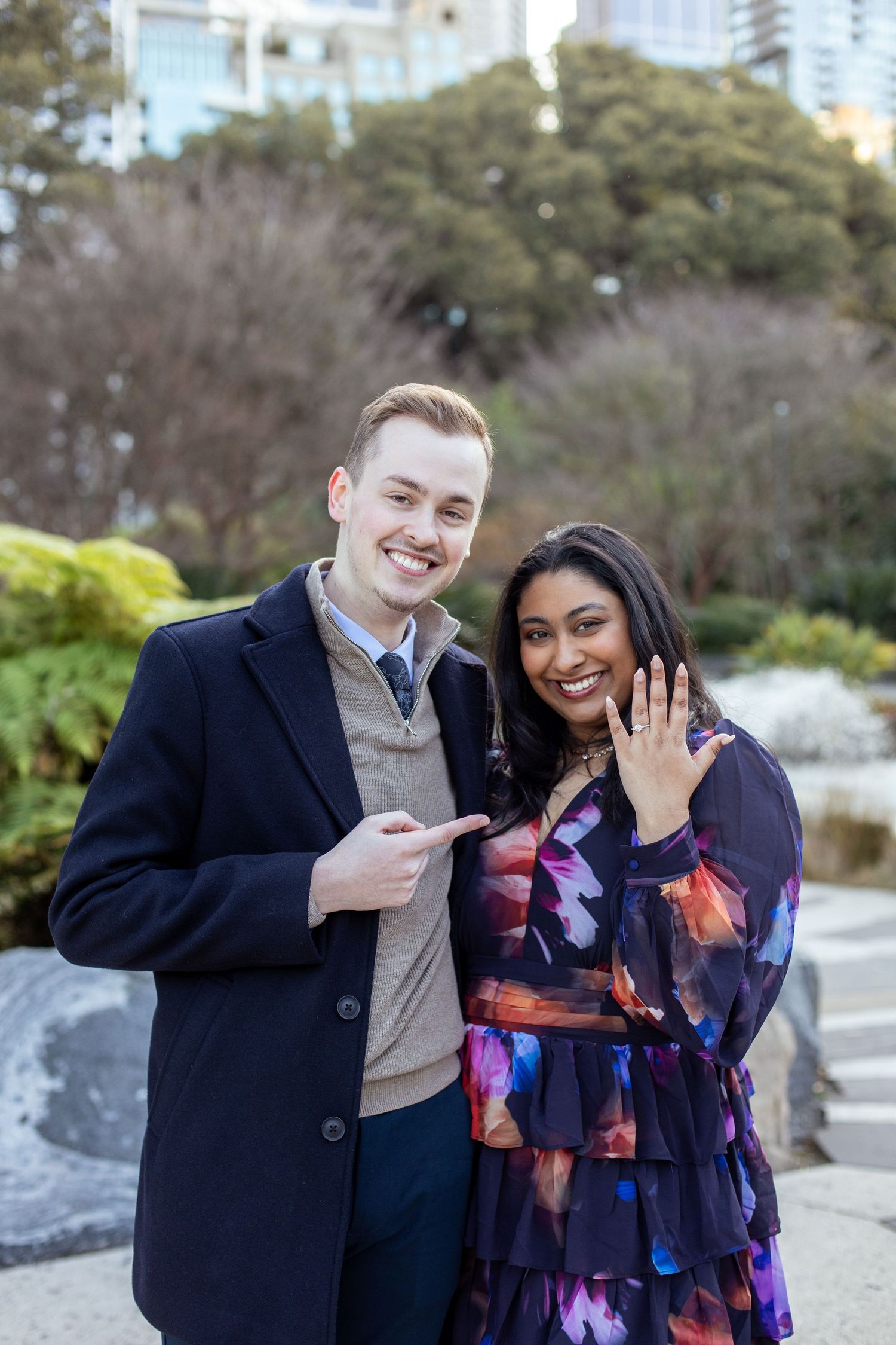 Newly engaged couple displaying the engagement ring in the picturesque Treasury Gardens, Melbourne, capturing a joyful moment of love.