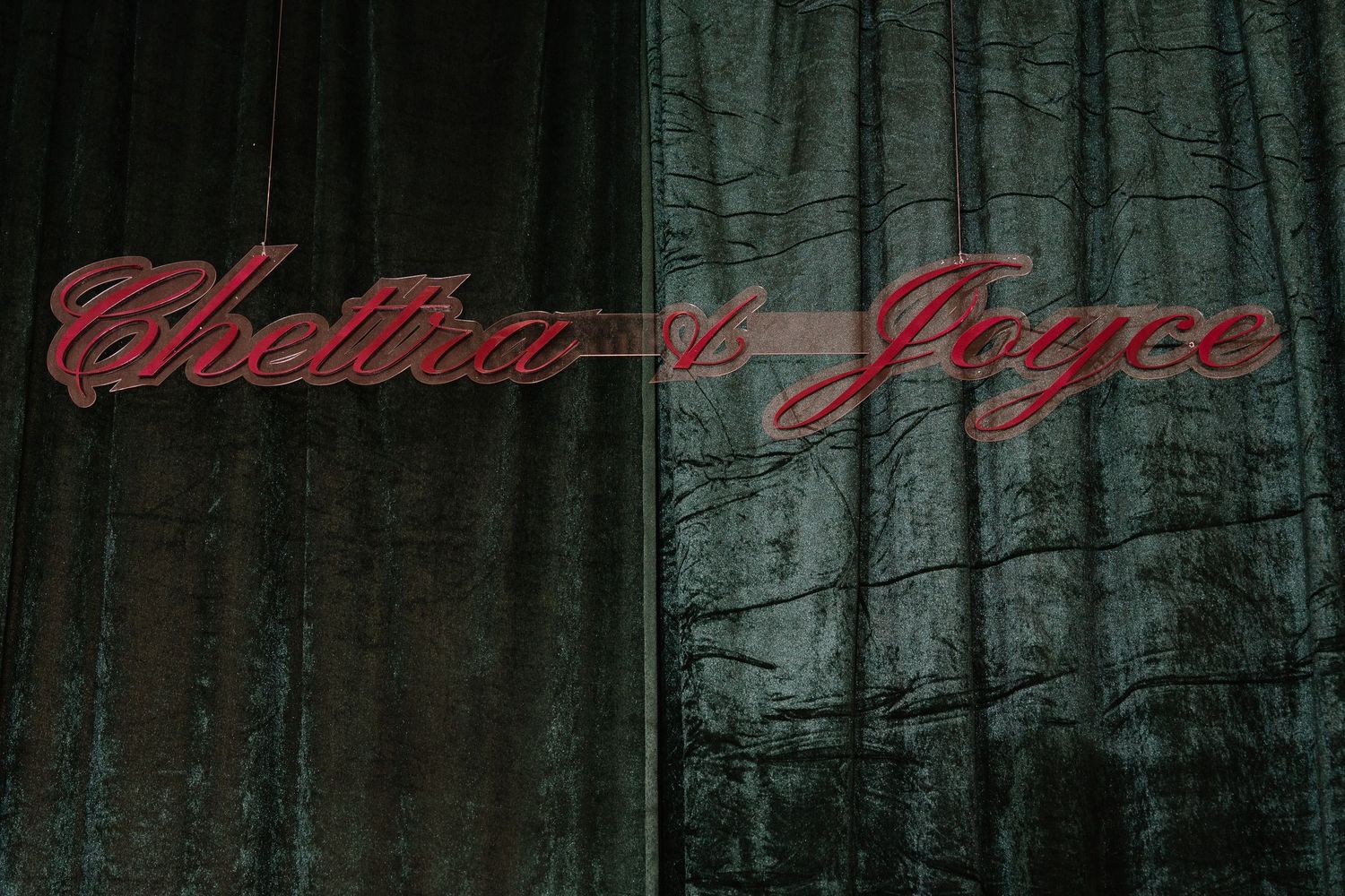 Elegant cursive Chettra and Joyce names displayed on dark green velvet curtain backdrop.