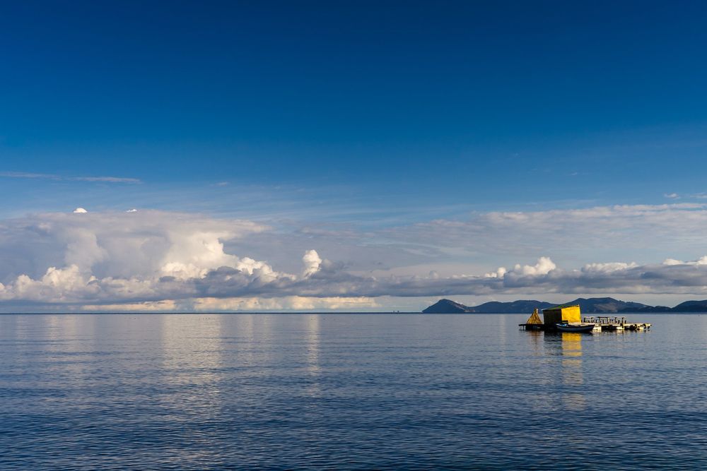 Serene ocean views with offshore oil platform and scattered clouds reflecting on calm blue waters at sunrise.