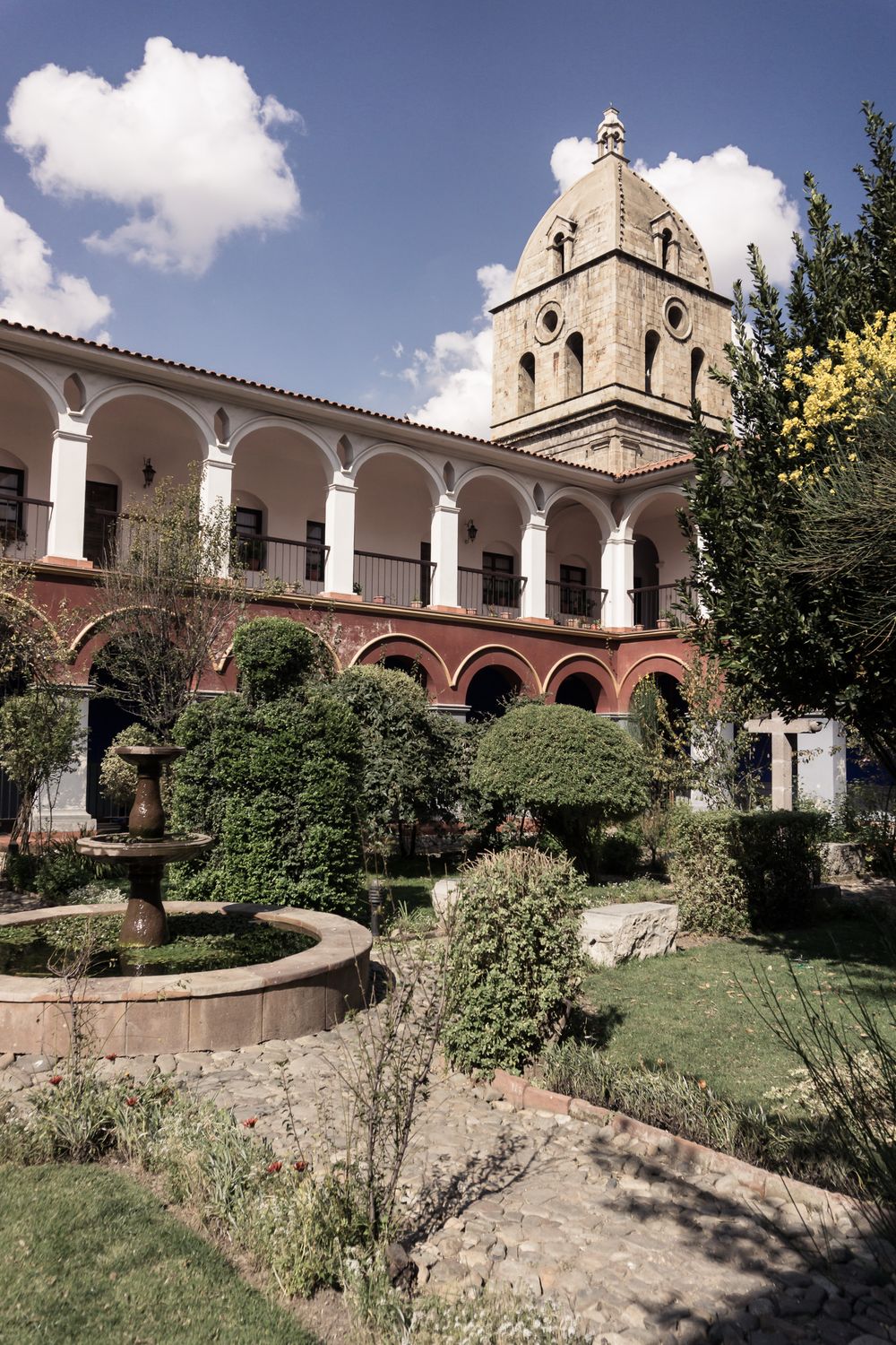 Historic Spanish colonial architecture features arched walkways and stone walls along a landscaped courtyard at a mission building.