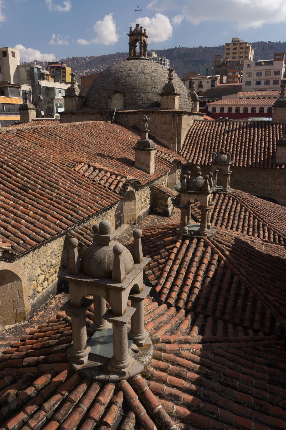 Terracotta roof tiles and historic stone chimneys on buildings in Florence, Italy, under a blue sky with white clouds.