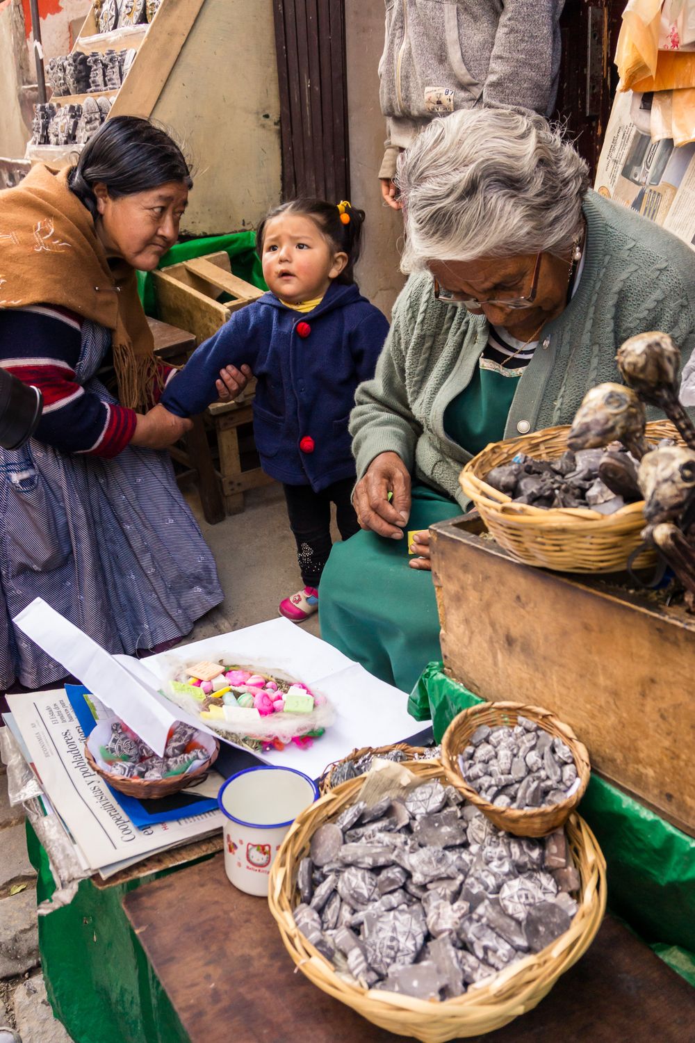 People examining traditional Chinese medicine ingredients in woven baskets at a local market stall.