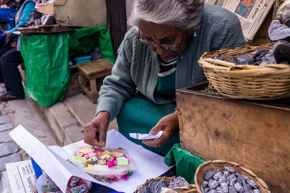 Artisans in green aprons carefully craft colorful paper flowers at a workshop table filled with supplies.