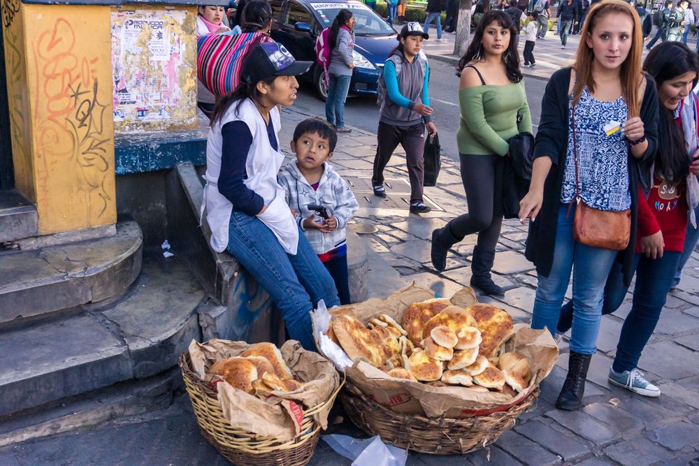 A busy street market scene with vendors selling bread and baked goods in large woven baskets.