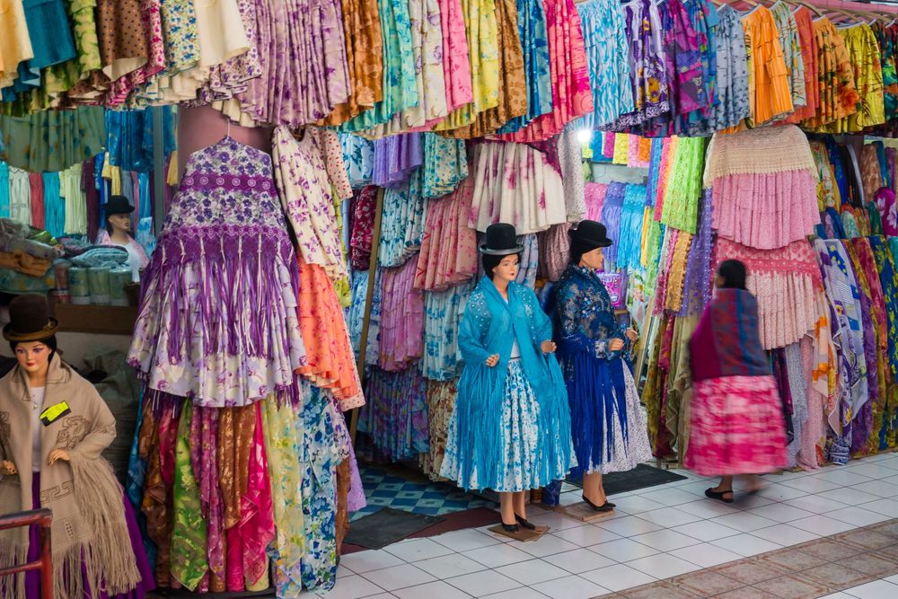 Rows of colorful traditional dresses and clothing hanging on display at a bustling market in Guatemala.