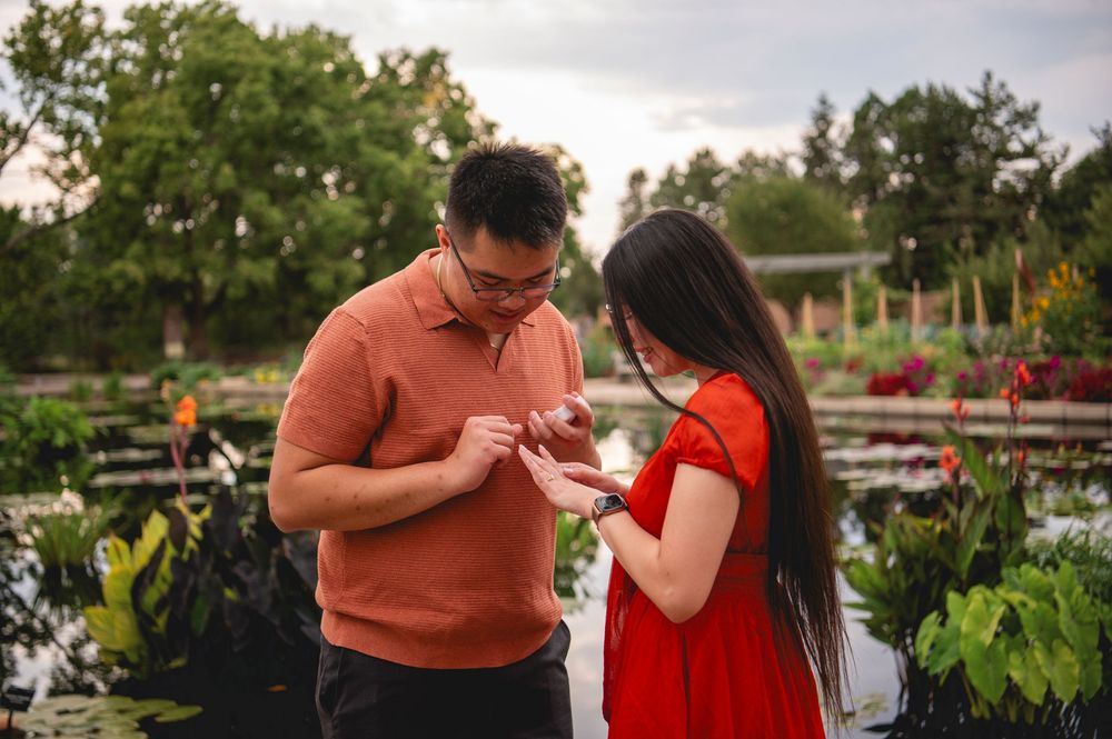 Couple in orange and red outfits sharing an intimate moment during an outdoor engagement photoshoot near a lake.