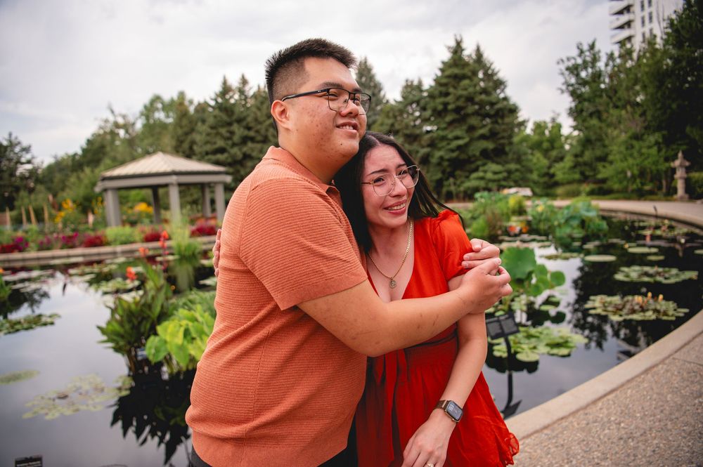 Happy couple sharing tender moments in a scenic garden walkway with tall buildings visible in the background.