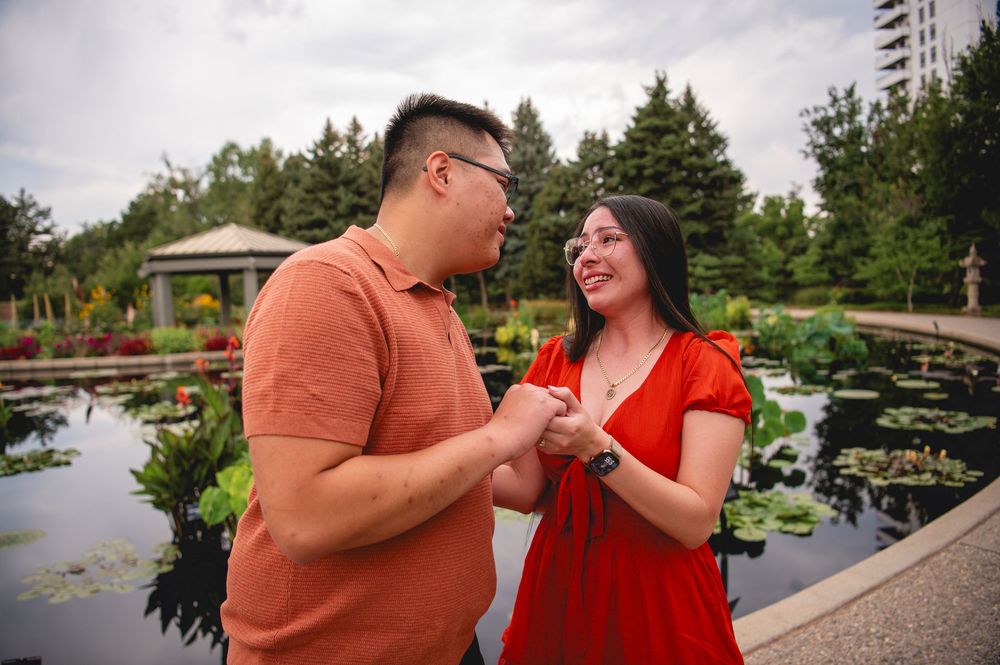 A couple shares romantic moments at a garden bridge with water and greenery in the background.