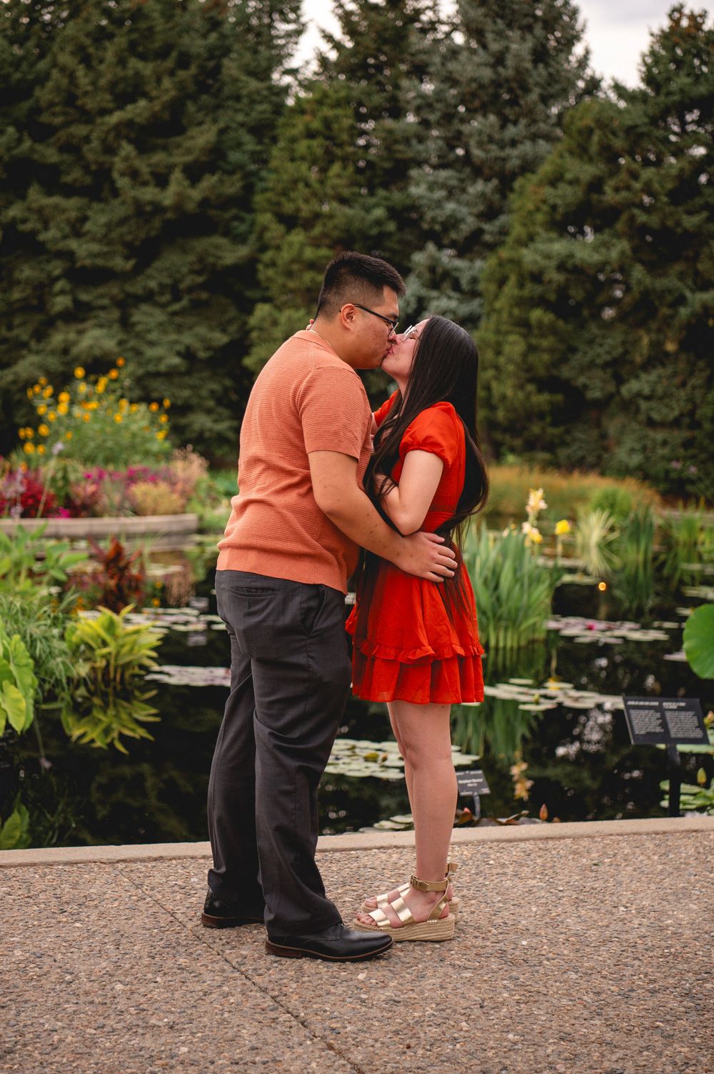 A couple shares a tender moment in a garden with blooming flowers and greenery in the background.