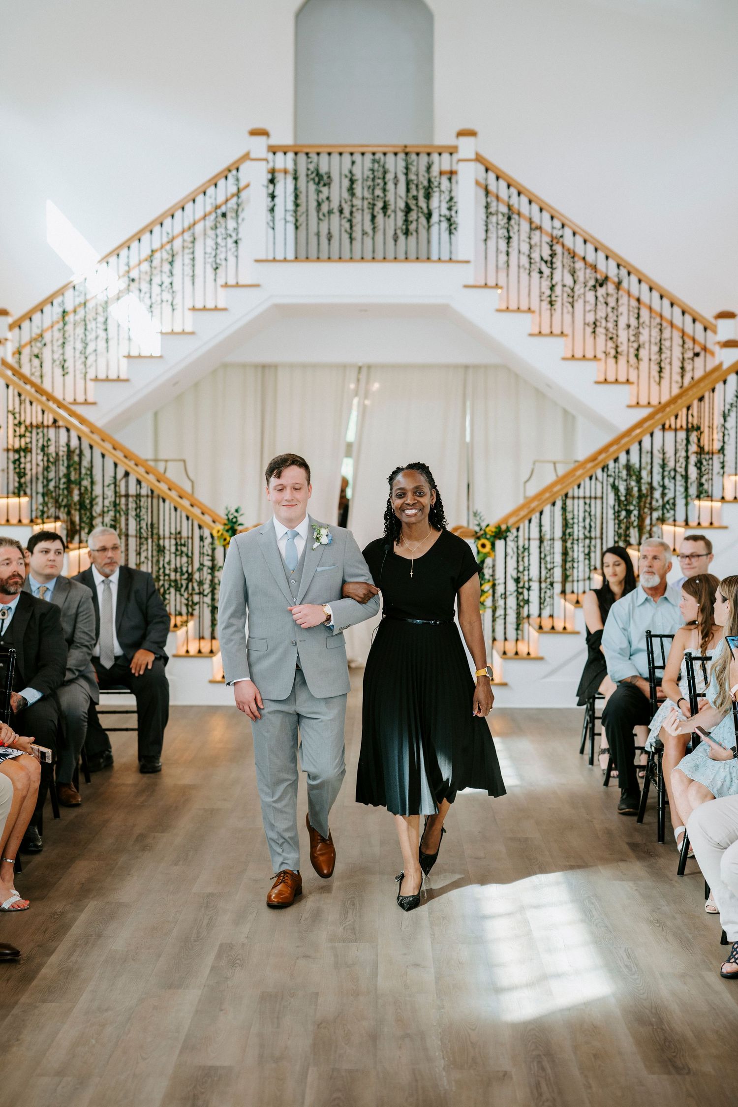 Wedding bridal party dancing together inside an elegant white venue with wooden staircase railings.