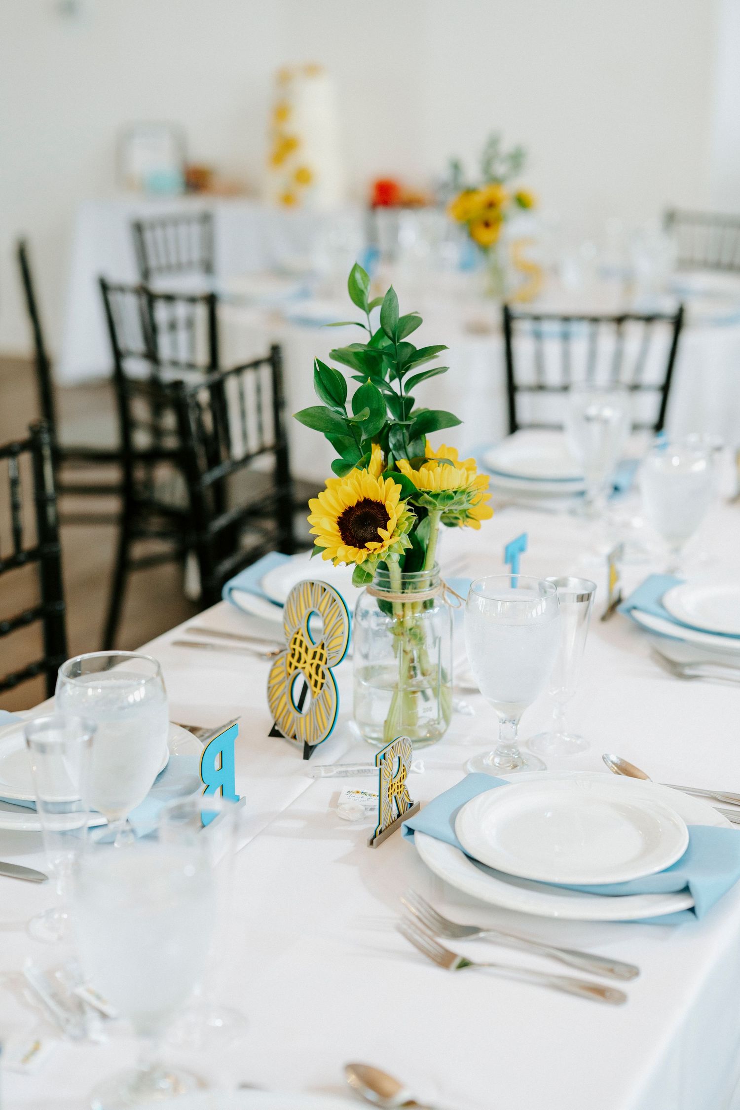 Elegant wedding reception tables with sunflower centerpieces, white linens and chiavari chairs set for a celebration.