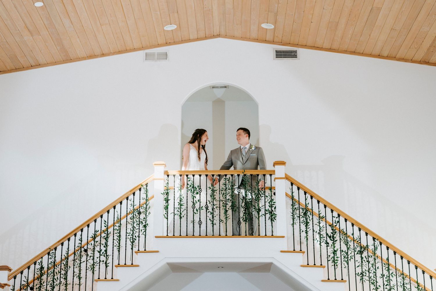 Modern wedding venue interior featuring wooden ceiling beams and ornate staircase railing.