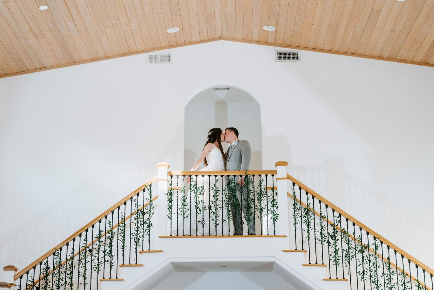 Wedding venue interior showing white walls, vaulted wooden ceiling, and decorative balcony railing.