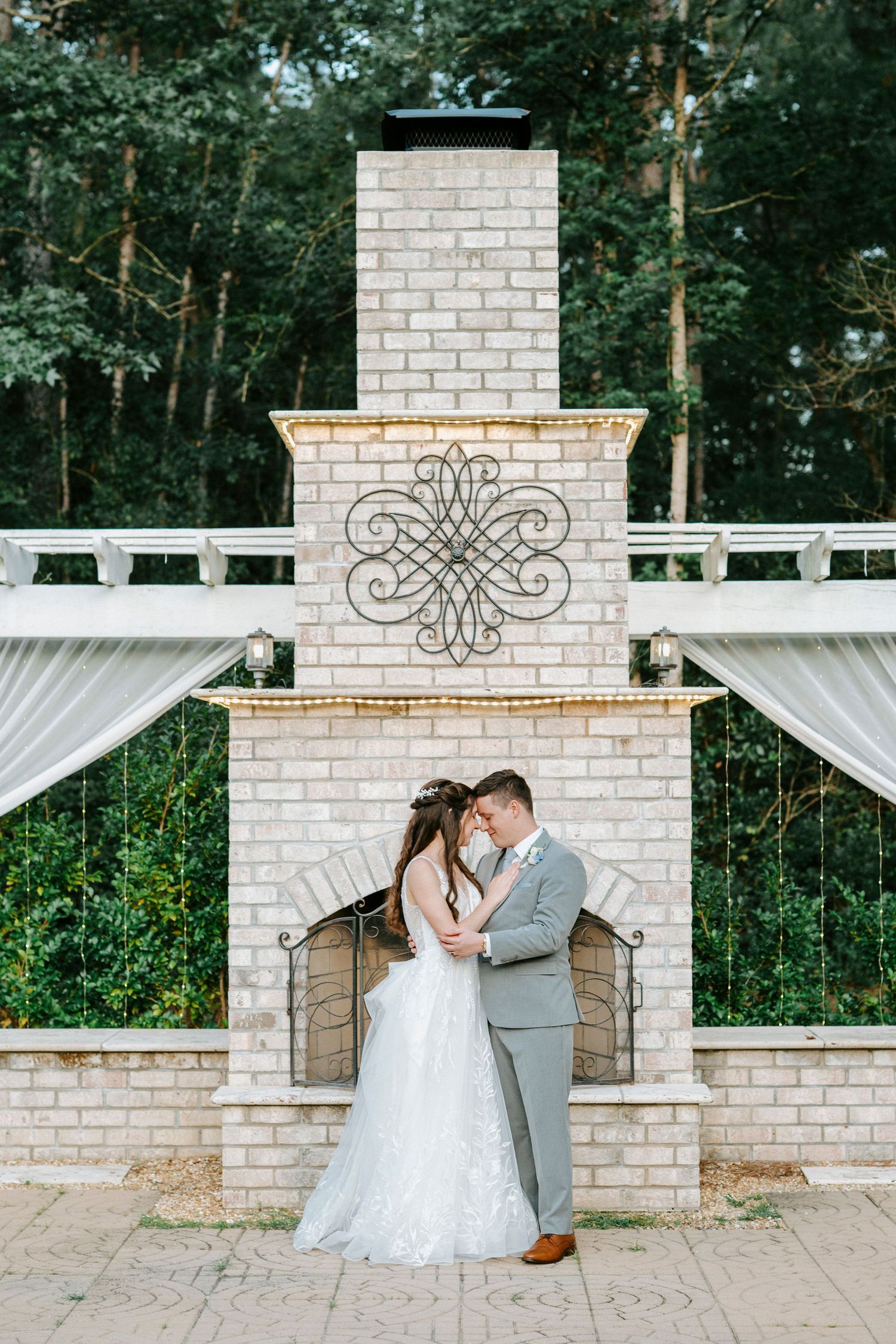 Wedding couple shares romantic moment by elegant white brick columns at outdoor garden ceremony location.