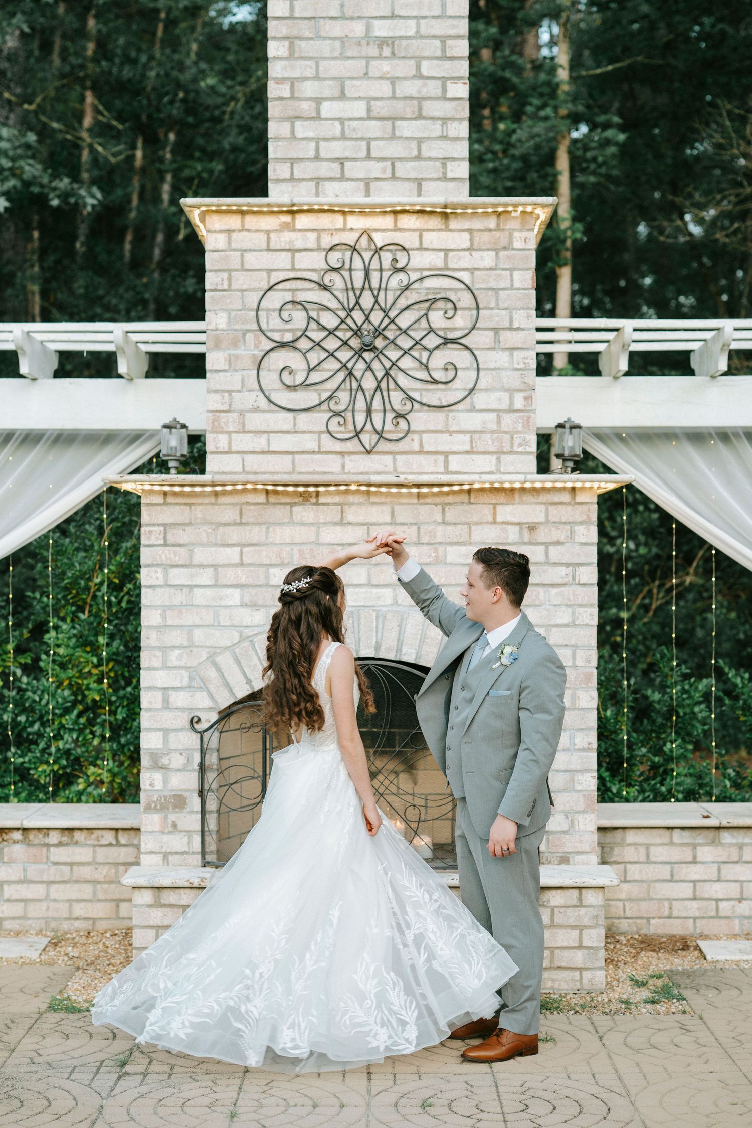 A couple poses in front of a decorative white brick fireplace with wrought iron details.