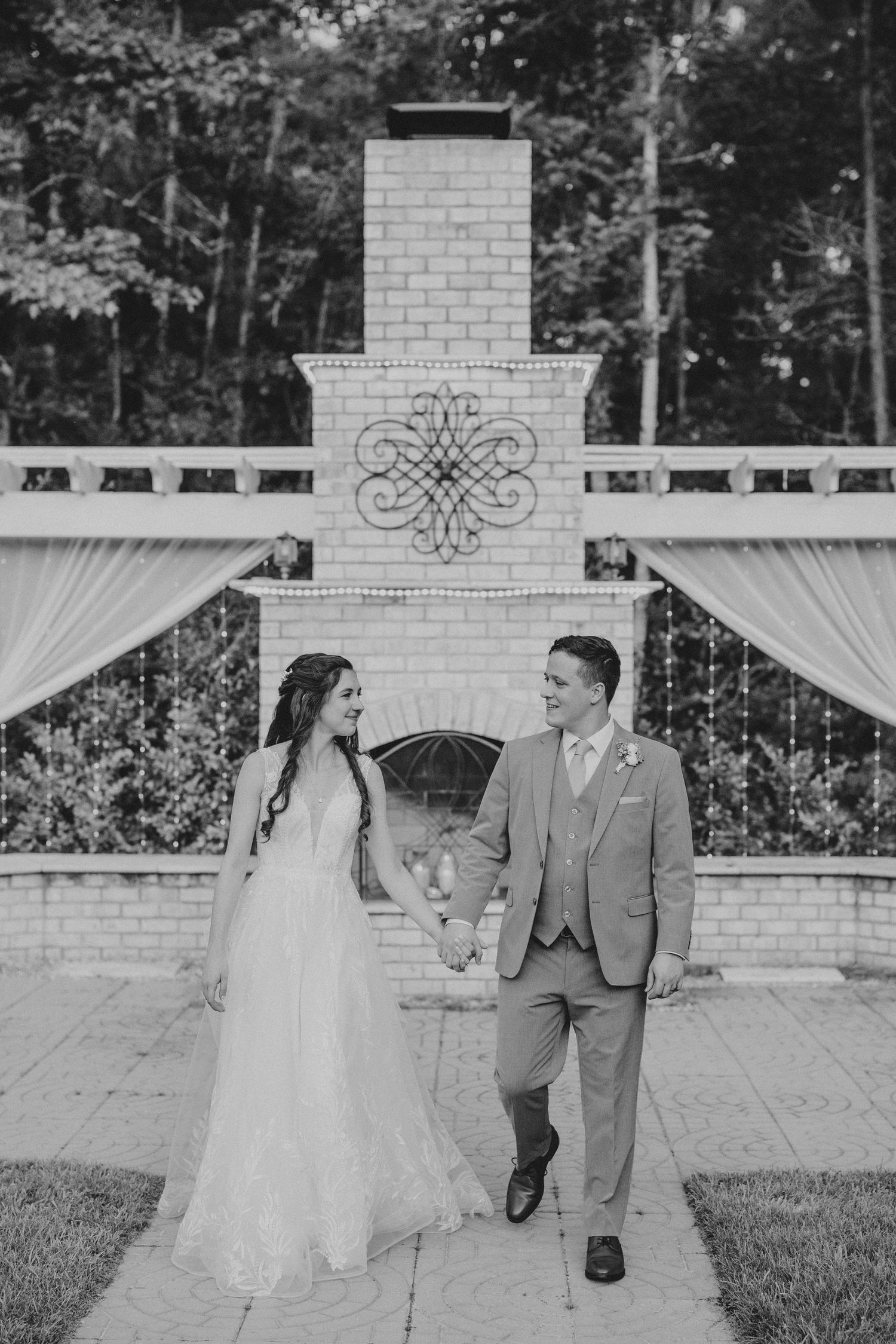 A couple poses for romantic black and white portraits in front of a white brick exterior with draped fabric decor.