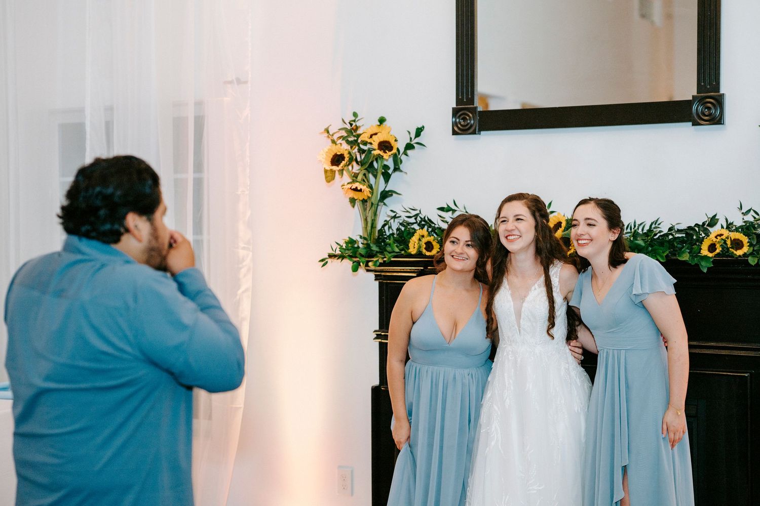 Blue-clad bridesmaids on a white dance floor shimmer under chandelier lighting at a joyful wedding reception.