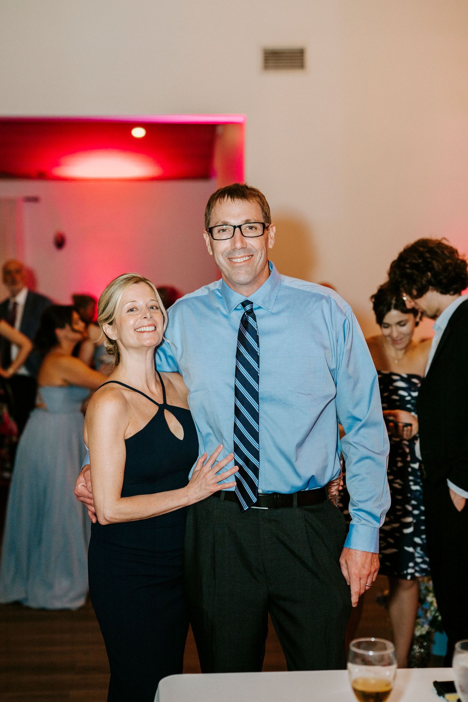 Guests dancing and socializing at an indoor wedding reception with red ambient lighting.
