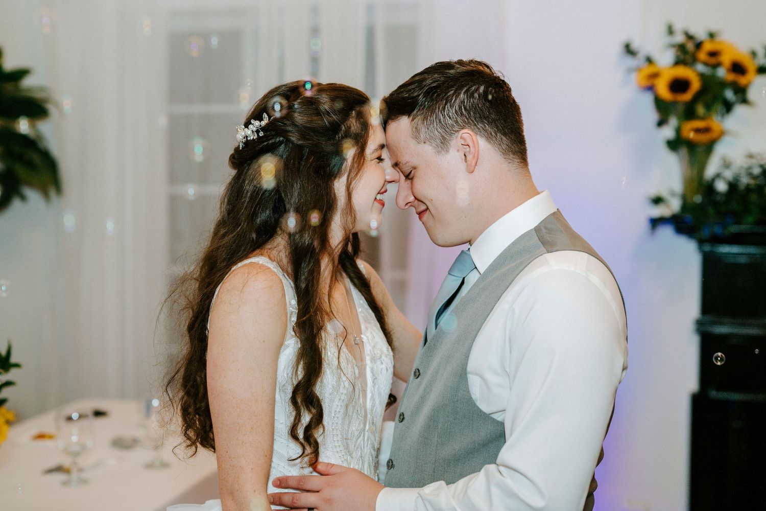 Wedding couple shares romantic moments in a venue decorated with bright sunflowers and greenery.