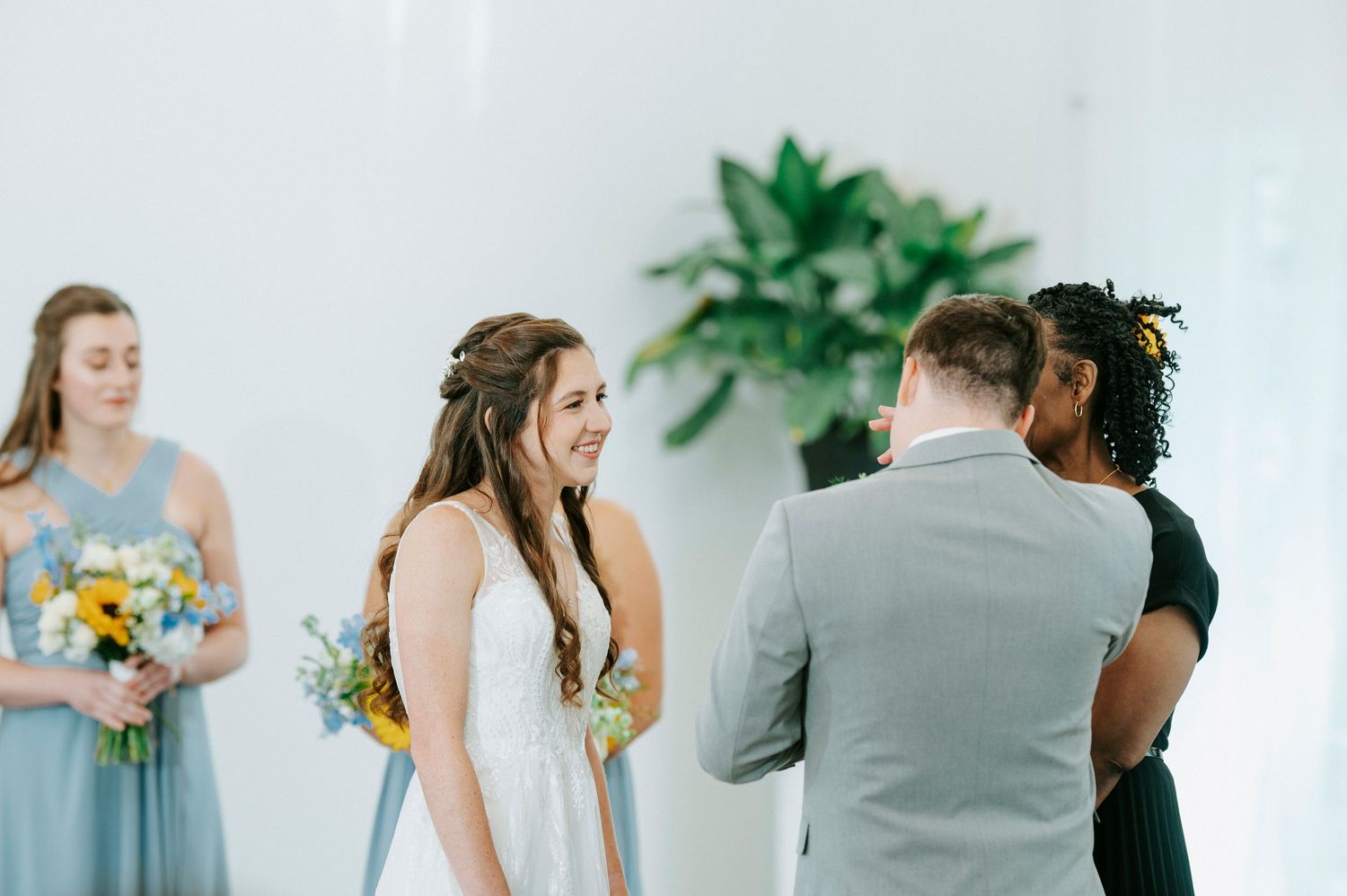 Elegant wedding party members pose during a bright indoor ceremony with greenery and floral decorations.