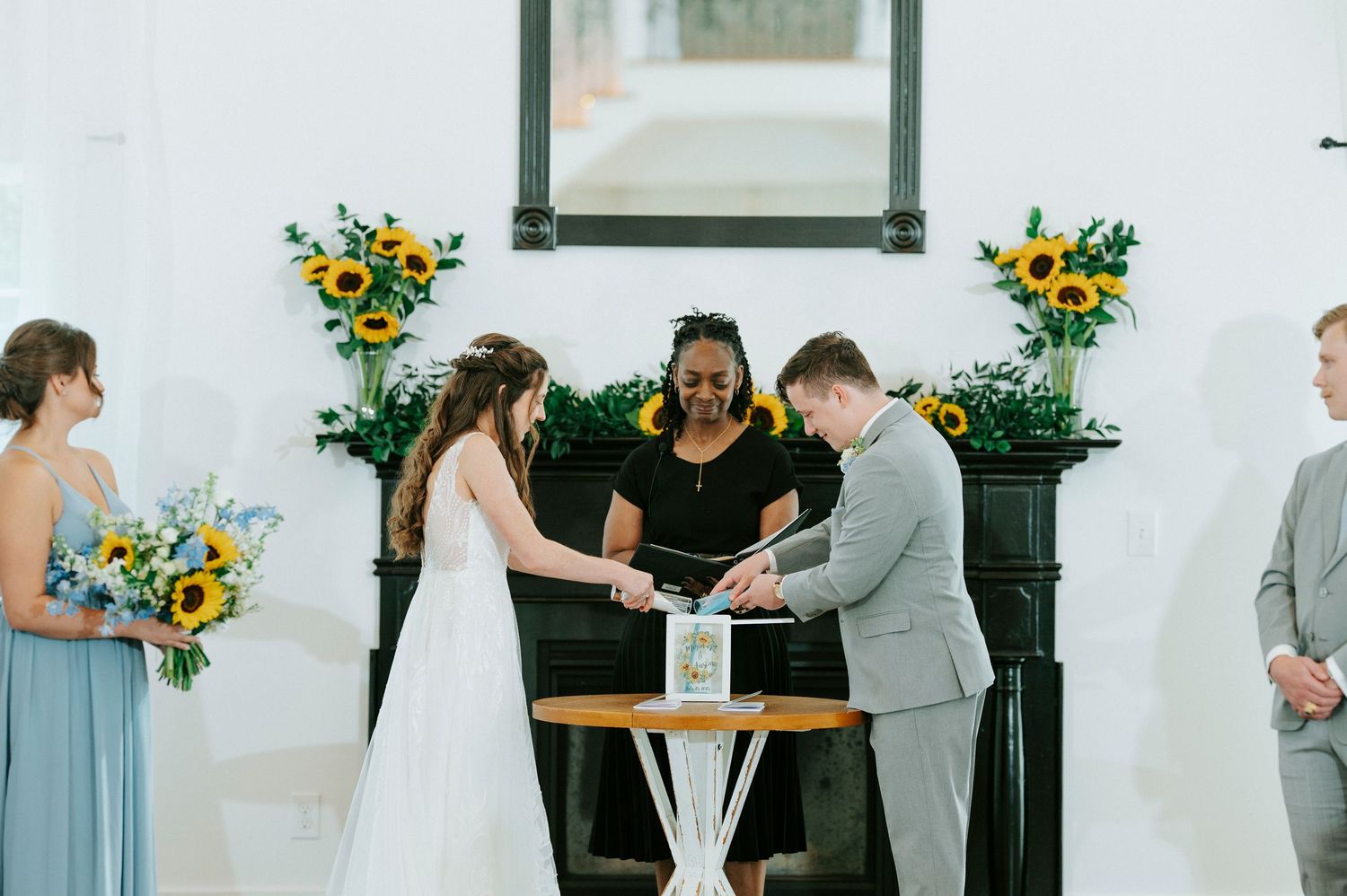 A wedding ceremony takes place outdoors with yellow sunflower arrangements and white decor.