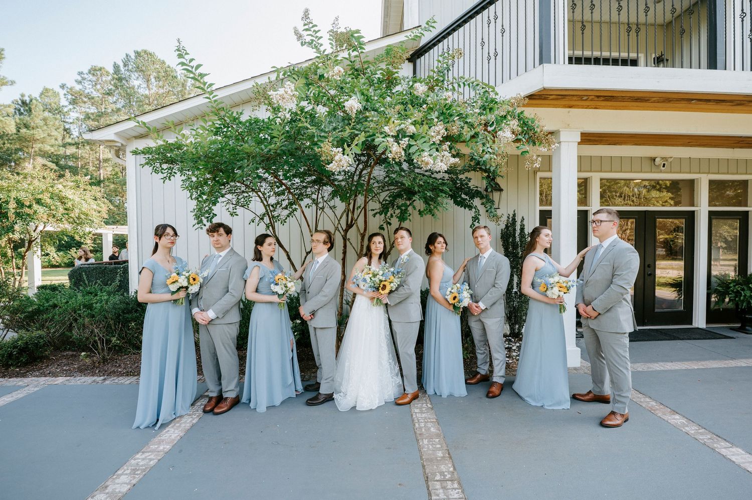 Wedding party in light blue dresses and gray suits posing outside a venue.