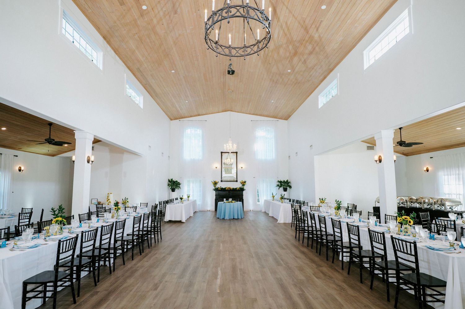Modern white wedding venue interior with wood ceiling, chandeliers and black chairs set up for ceremony.