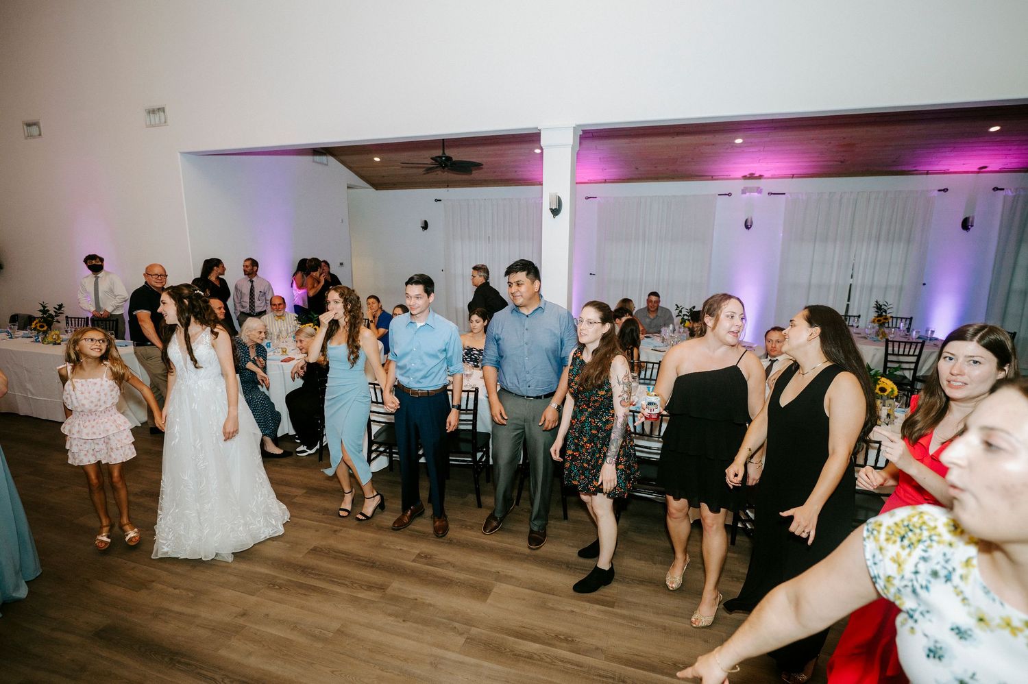 Wedding reception guests dancing and celebrating on a wooden dance floor in an event venue.