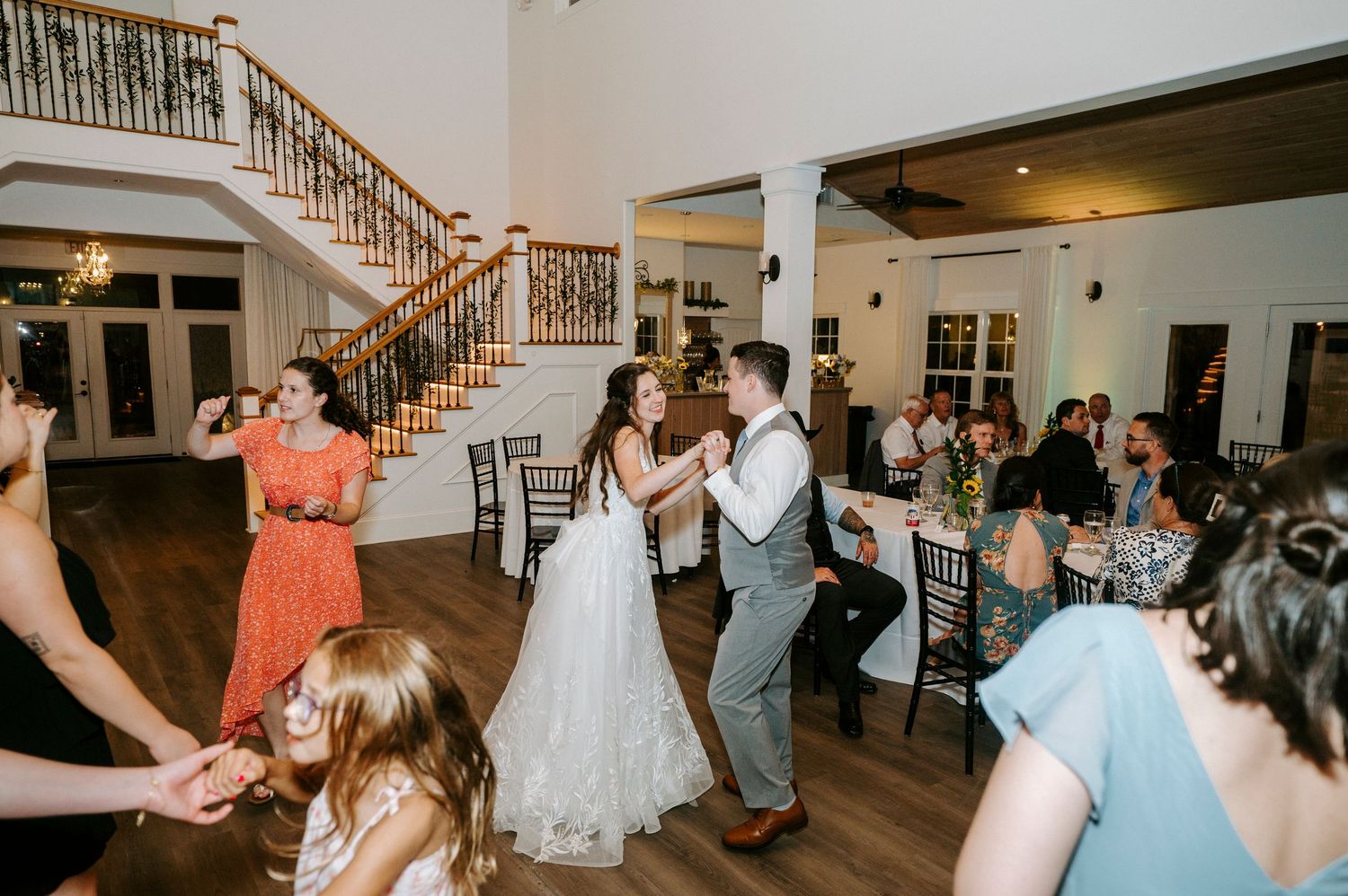 Elegant event space with wooden staircase and guests dancing at a reception party.