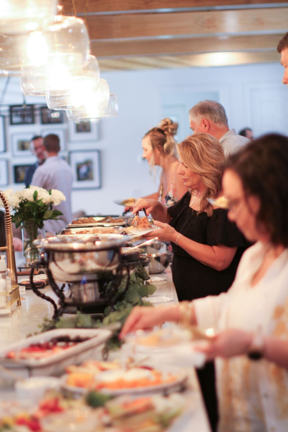 People enjoying food at a buffet dining setup with silver serving trays and decorative greenery.