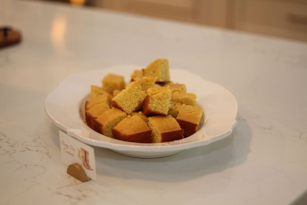 Golden brown cornbread squares are arranged on a white plate atop a light marble counter.