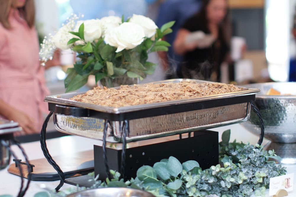 White floral centerpieces with greenery and potted plants line a long wooden dining table at an elegant event.