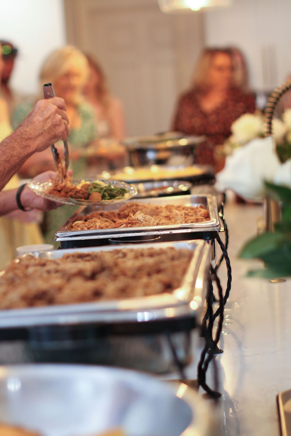 Close-up view of food being served in silver chafing dishes at a catered event buffet line.