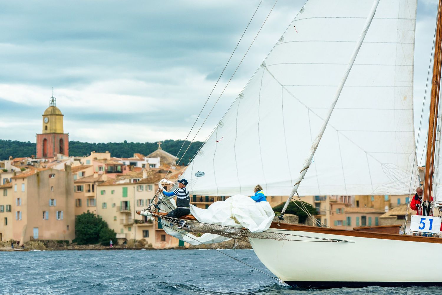 Sailboats glide across the Mediterranean waters near Saint-Tropez with the iconic church tower and coastal buildings visible.