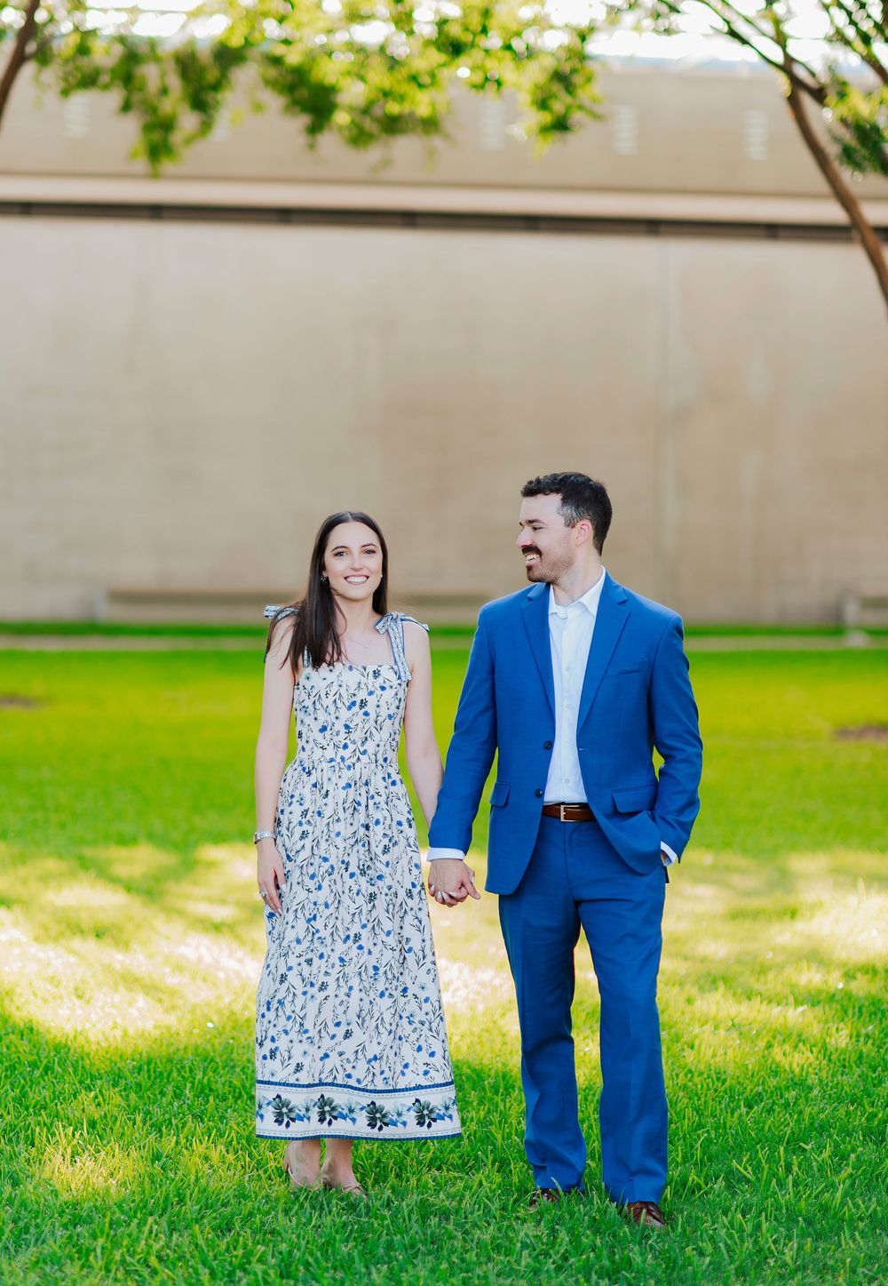A couple stands together on grass, wearing coordinated blue and floral outfits for their engagement photos.