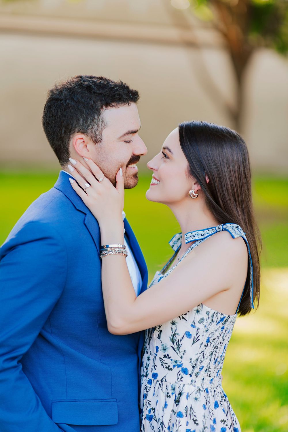 Romantic moment between couple in blue suit and floral dress against blurred garden background.