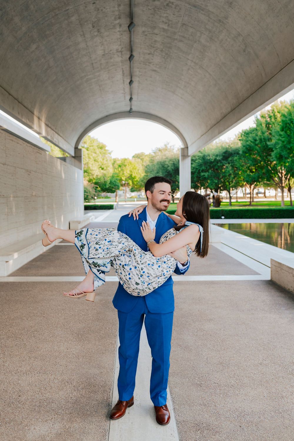A playful dip pose under an architectural archway with a park landscape in the background.