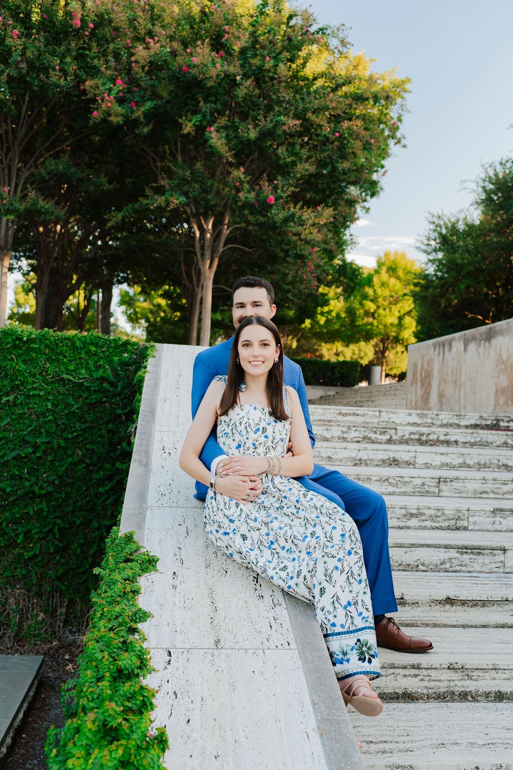 Couple in coordinated blue outfits sitting on concrete steps surrounded by lush greenery.