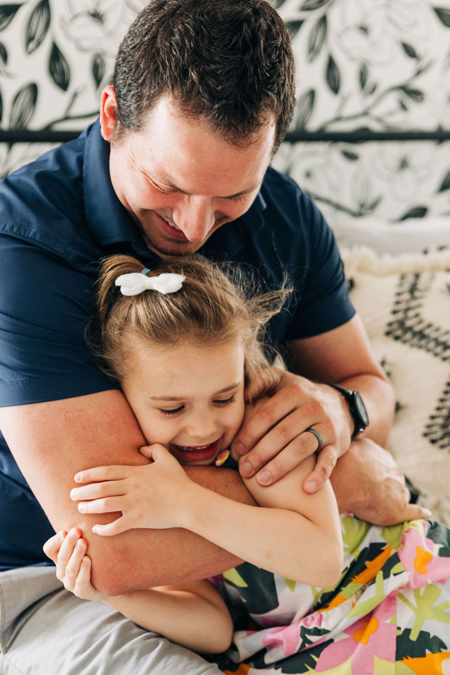 A heartwarming moment shows playful tickling and laughter on a floral patterned couch between dad and daughter