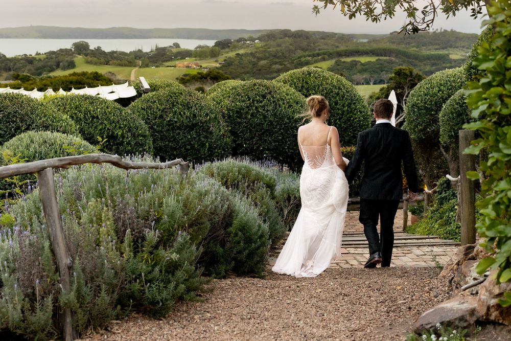 Wedding couple walks along a garden path surrounded by lavender and greenery.