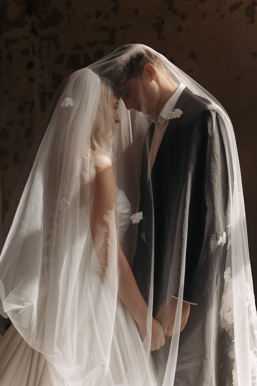 A romantic wedding moment captured through a flowing white veil as a couple shares a tender kiss.