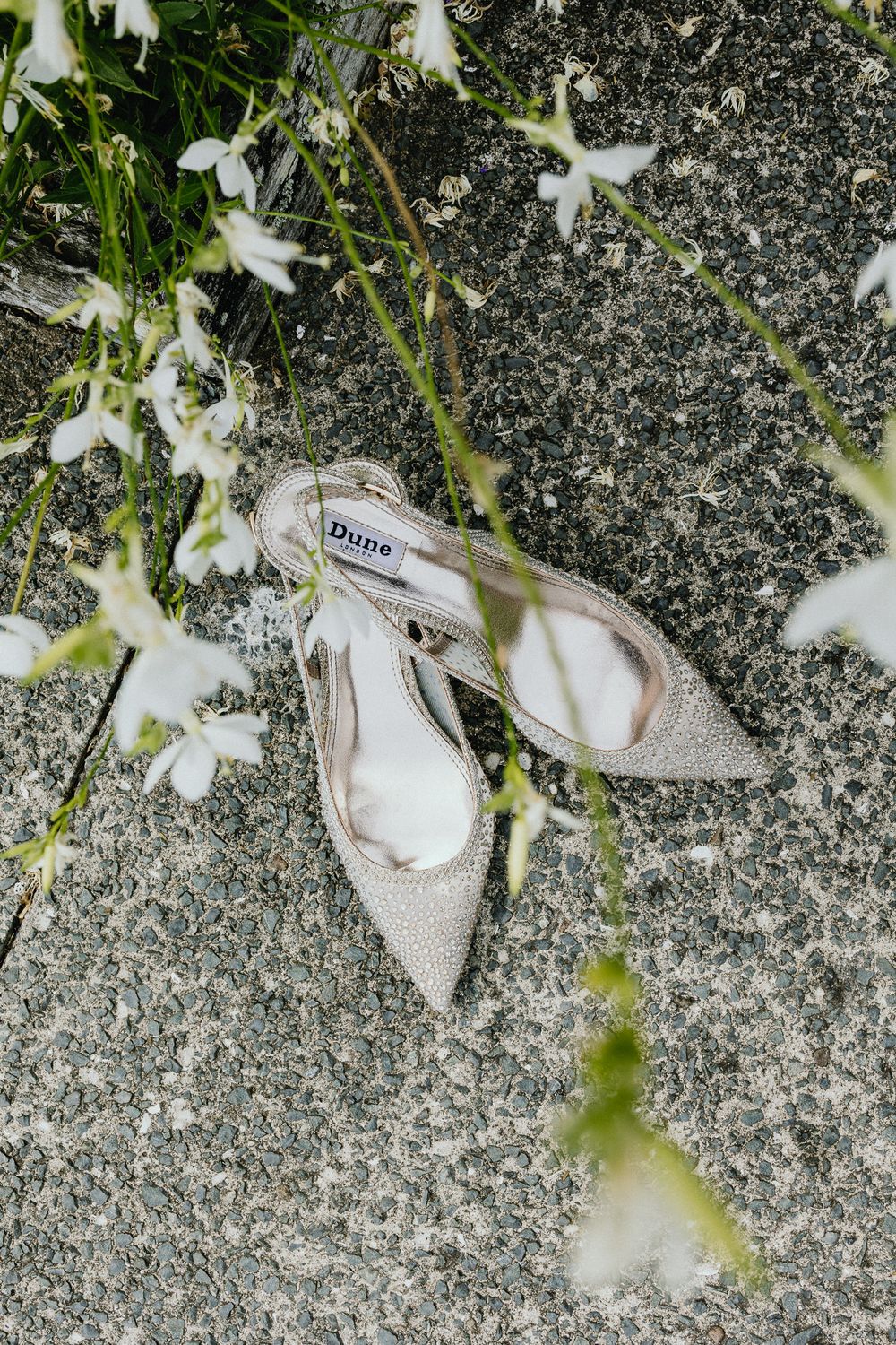 White bridal shoes rest elegantly against a stone surface surrounded by delicate white flowers.