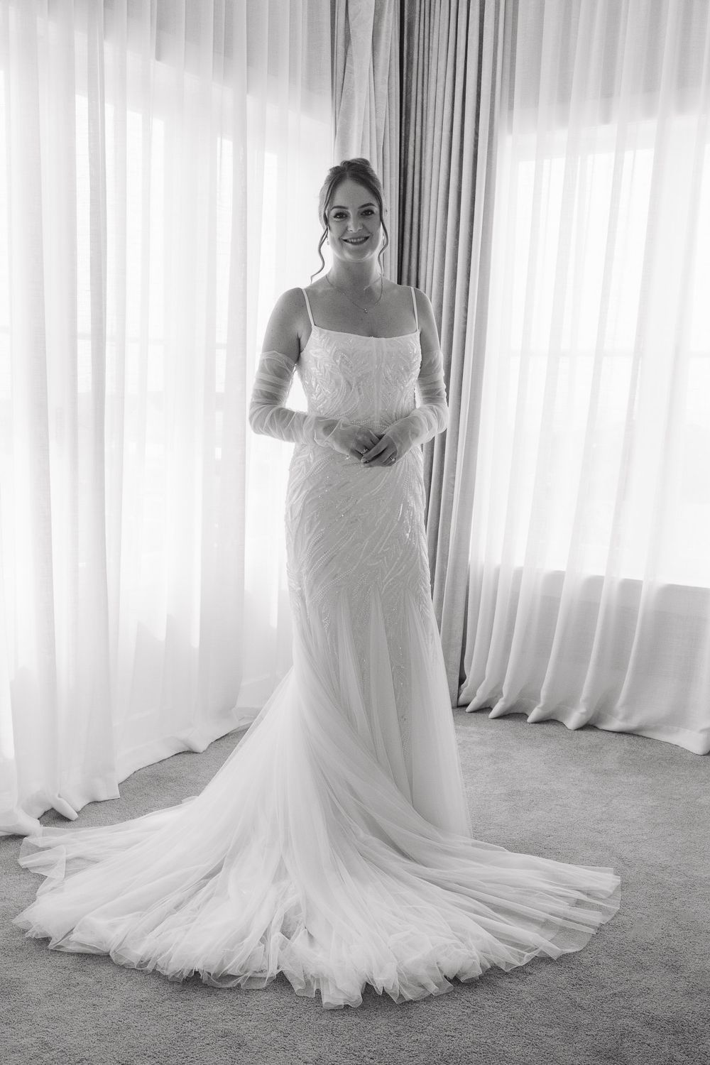 A flowing white wedding gown with a dramatic train photographed in a bright room with sheer curtains.