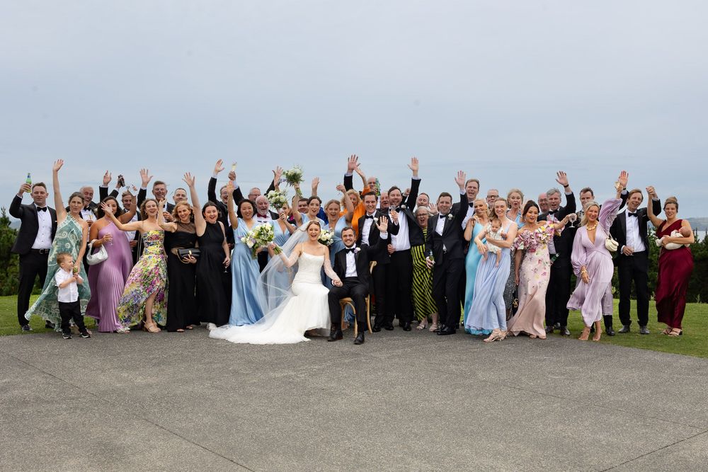 Large group of wedding guests pose together outdoors for a celebratory photo.