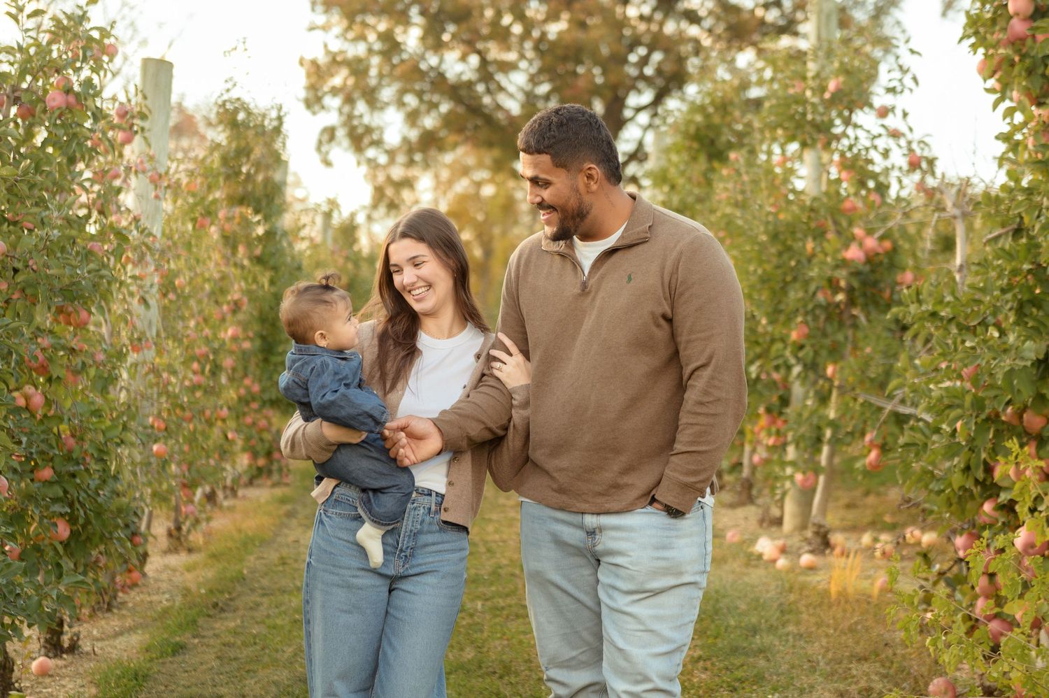 A family enjoys a sunny autumn day walking together through an apple orchard with golden foliage.